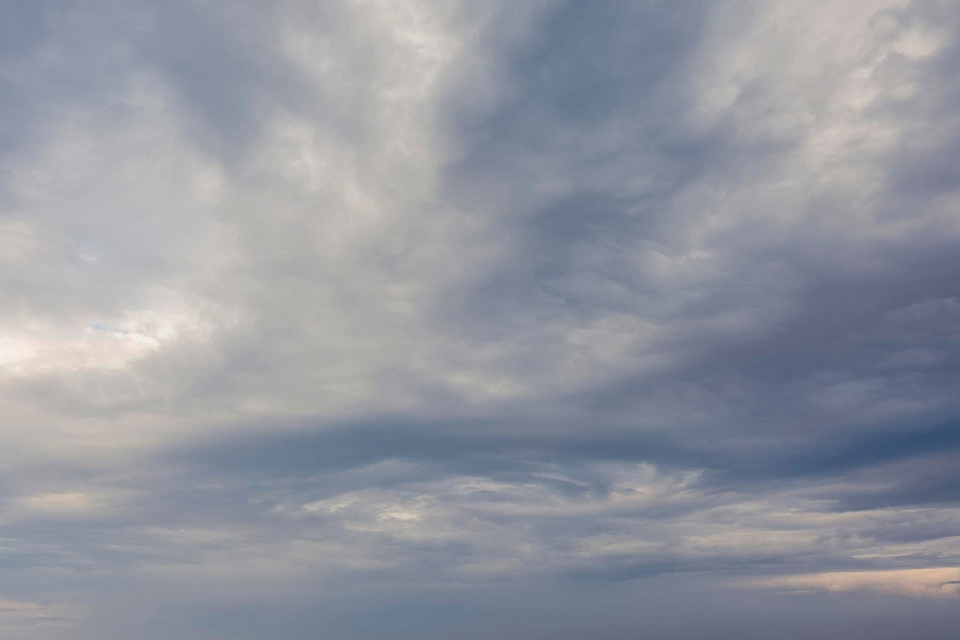 A dense expanse of stratified, undulating clouds rendered in a muted palette of slate blue, dove gray, and soft cream.